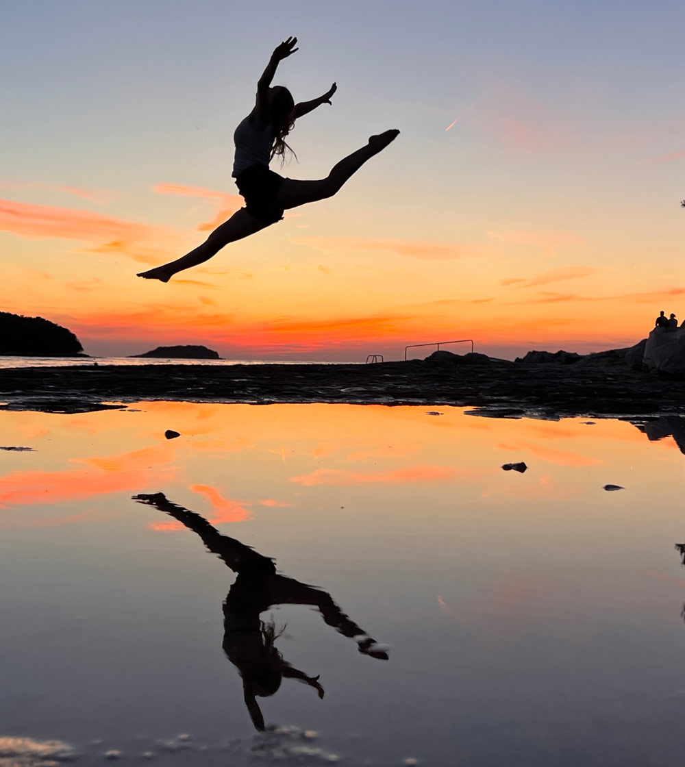 Silhouette einer Frau im Freudensprung am Meer bei Sonnenuntergang, als Symbol für emotionale Freiheit und Leichtigkeit nach Emotionscode® Sitzung. Das emotionale Gepäck wurde abgestellt und es kann wieder frei durchgeatmet werden.