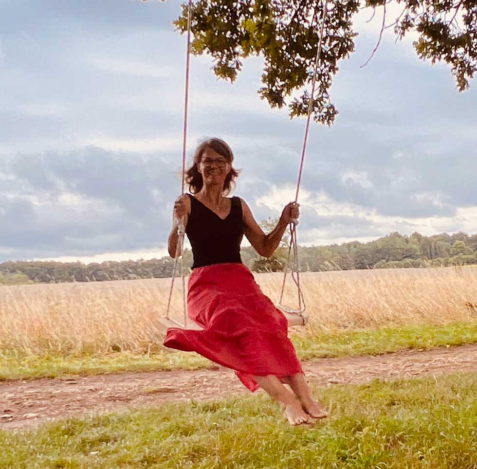 Frau auf einer Holzschaukel an einem kräftigen Baum, als Symbol für Freiheit, Leichtigkeit, Selbstverwirklichung und die Wirkung des Belief Code®.