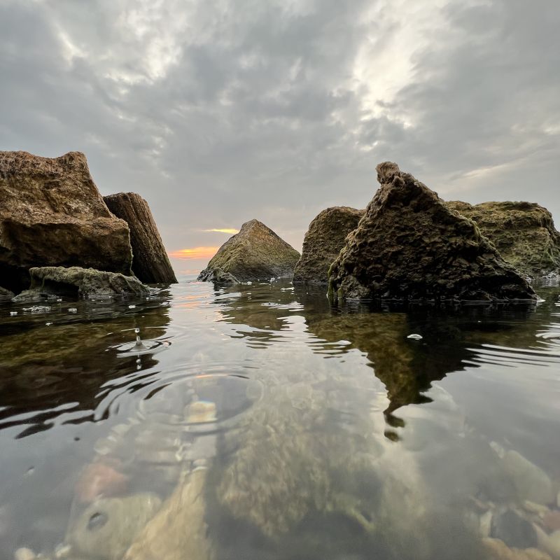 Felsen im stillen Wasser bei Sonnenuntergang mit Spiegelung – Symbol für innere Balance und die Erkenntnis, dass die Lösung oft woanders liegt als wir denken