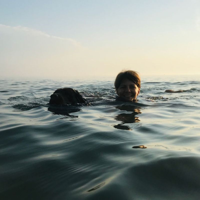 Mensch und Hund schwimmen nebeneinander im Meer, nur ihre Köpfe sind über der Wasseroberfläche zu sehen. Ein Zeichen von Vertrauen, Verbundenheit und gemeinsamer Stärke.