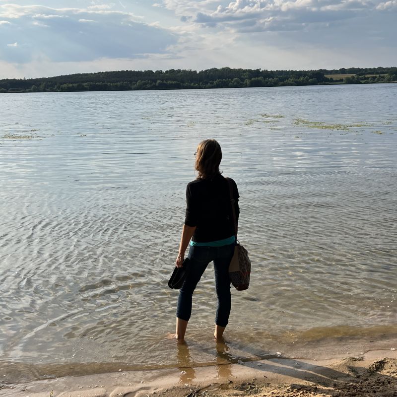 Frau steht allein am See und schaut in die Weite – Stille und Selbstreflexion