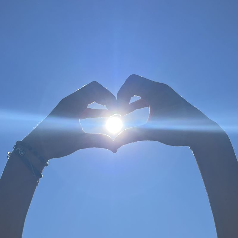 Hände formen ein Herz vor blauem Himmel mit Sonne – Glücklichsein als Geburtsrecht
